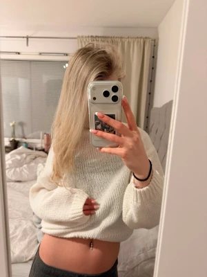 Vit cropped stickad tröja - Säljer en vit cropped stickad tröja med avslappnad passform och långa ärmar. Tröjan har breda muddar vid ärmslut och nederkant, samt en mjuk och luftig struktur. Perfekt för lager på lager och chill dagar.