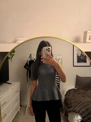 Grå stickad peplumtop från H&M - Superfin grå stickad peplumtop från H&M med korta ärmar och rund hals. Toppen har en markerad midja och volang nertill som ger en snygg siluett. 