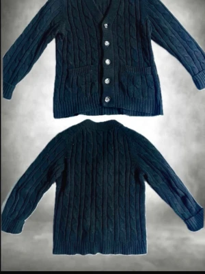 Mörkblå kabelstickad kofta - Kabelstickad kofta i mörkblått med v-ringning och fem knappar framtill. Tröjan har två fickor fram och ribbade muddar vid ärmslut och nederkant. Perfekt för lager på lager under kyliga dagar.