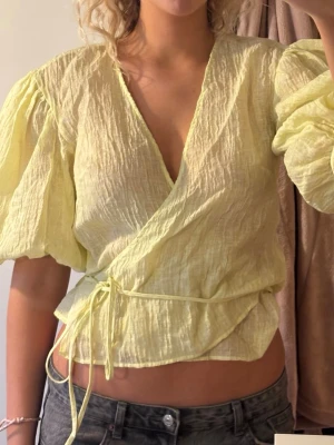 Gul omlottblus med puffärm - Trendig gul omlottblus från H&M med puffiga trekvartsärmar och knytband i midjan. Jag är 180cm lång och bär vanligtvis S/M. Skicka gärna frågor eller prisförslag!