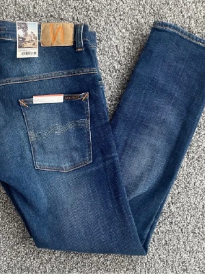 Blå Nudie Jeans  - Säljer ett par klassiska blå jeans från Nudie Jeans. Jeansen har en snygg tvätt, fem fickor och kontrastsömmar. Finns i flera storlekar!!