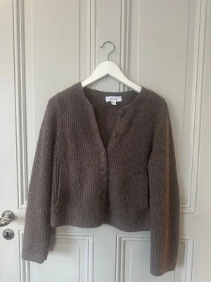 Brun ribbad kofta från & Other Stories - Mysig brun kofta från & Other Stories i ribbstickad ullmix. Modellen har v-ringning, knappar framtill och två fickor. Perfekt för lager på lager under höst och vinter. Klassisk och enkel design som är lätt att matcha.