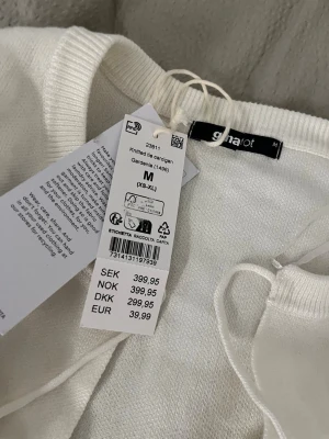 Vit stickad kofta från Gina Tricot - Vit kofta ifrån Gina med tre rosetter som knyts framtill, helt ny endast testad, säljer då den aldrig kommer till användning