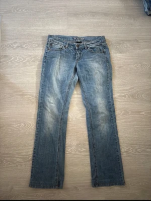 Blå jeans från Two Days Later - Säljer ett par klassiska blå jeans från Two Days Later, modell straight fit med normal passform. Jeansen har fem fickor, knappgylf och snygga slitningar framtill. Perfekta till vardagslooken och tillverkade i slitstarkt bomullsmaterial.