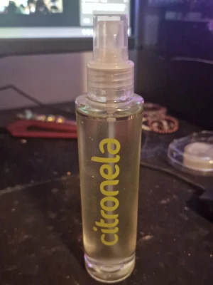 Citronela parfym sprayflaska - Fräsch parfym i genomskinlig glasflaska med sprayfunktion från Citronela. Flaskan är cylindrisk och har gul text på framsidan. Innehållet är ljusgult och flaskan har en modern, enkel design.