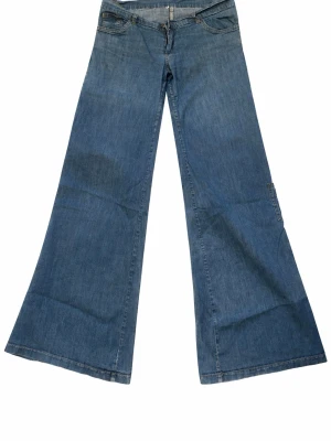 Blå wide jeans med utsvängda ben - Säljer ett par blå wide jeans med riktigt utsvängda ben och låg midja. Klassisk femficksmodell i mjukt denimtyg, perfekta för dig som gillar retrovibbar och vill sticka ut. Passar till sneakers eller boots för en cool look. Köpta under 90-00 talet. Y2K