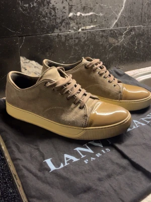 🤎 Lanvin Paris sneakers – mocka & lacktå - Exklusiva Lanvin Paris sneakers i mocka med ikonisk lacktå. Lyxig design med perfekt balans mellan dressat och casual. Väldigt eftertraktad modell som funkar lika bra till jeans som kostymbyxor. Levereras med original dustbag. Låda följs såklart med också