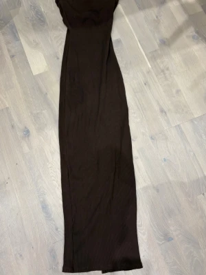 Brun ribbad långkjol - Säljer en brun ribbad långklänning i stretchigt material. Klänningen har en rak passform och en slits på sidan som ger en snygg detalj. 