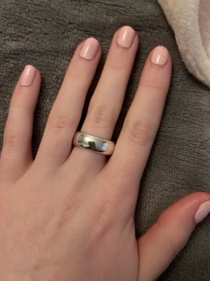 Klassisk bred silverring - Säljer en stilren och klassisk bred ring i silverfärgat material. Ringen har en slät, blank yta och rundad form som ger en tidlös look. Perfekt för dig som gillar minimalistiska accessoarer och vill ha något som passar till många olika stilar.Vid köp av fler ringar kan jag slå ihop annonserna så frakten blir billigare.