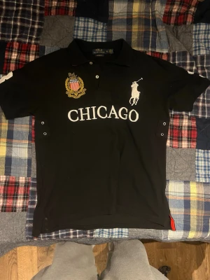 Svart piké Polo Ralph Lauren XL - Säljer en svart pikétröja från Polo Ralph Lauren i storlek XL. Tröjan har broderad logga, texten CHICAGO framtill och en stor vit siffra 3 på ryggen. Klassisk krage, korta ärmar och detaljer i vitt och gult. Custom fit-modell i mjuk bomull.