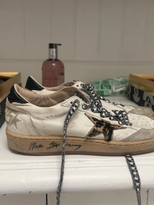 Golden Goose sneakers med leopardstjärna - Snygga vita sneakers från Golden Goose med svart häl, leopardmönstrad stjärna på sidan och svarta/vita snören. Skorna har rund tå, platt sula och coola detaljer som text på sulan. Perfekta för dig som gillar unik stil.