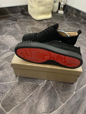 Svarta Louboutin sneakers med nitar - Säljer ett par svarta sneakers från Christian Louboutin med mattsvarta nitar på tån och den klassiska röda sulan. Har tappat några spikar men det är ingenting som märks av.