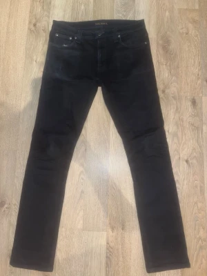 Svarta jeans från Nudie Jeans Co - Snygga svarta jeans från Nudie Jeans Co med klassisk femficksdesign och raka ben. Jeansen har normal passform och är tillverkade i mjukt bomullsmaterial. Perfekta för dig som gillar stilrena och tidlösa plagg.