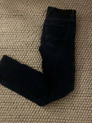 Mörkblå Replay jeans straight fit - Säljer ett par mörkblå jeans från Replay med klassisk femficksmodell och raka ben. Jeansen har kontrastsömmar och Replay-logga på bakfickan. Perfekta för dig som gillar en enkel och tidlös stil.