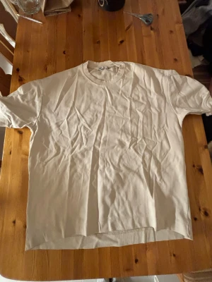 Vit basic t-shirt i bomull - Enkel vit t-shirt med rund hals och korta ärmar. Tillverkad i mjuk bomull, perfekt för en clean och avslappnad stil. Passformen är klassisk och t-shirten är helt utan mönster eller tryck.