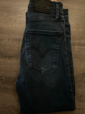 Levi's 511 mörkblå jeans herr - Mörkblå Levi's 511 jeans med klassisk femficksdesign och svarta detaljer på bakfickan. Jeansen har en slim passform och är tillverkade i mjukt denimtyg av bomull. Perfekta för dig som gillar en stilren och tidlös look. Lite slitet vid ficka.