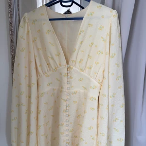 Blommig ljus klänning från Adoore - Supersöt ljusgul klänning från Adoore med små gula blommor, djup v-ringning och klädda knappar framtill. Långärmad modell i ett lätt, strukturerat tyg som känns perfekt för vår och sommar. Romantisk och feminin vibe! Använd 1 gång, 1300kr. Accepterar ej bud under 1100 pga otroligt många skambud.