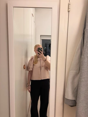 Ljusrosa puffärmad blus med rosett - Supersöt ljusrosa blus med korta puffärmar och dekorativa rosetter framtill. Blusen har en boxig passform och är tillverkad i ett glansigt, satinliknande material som ger en lyxig känsla. Perfekt för dig som gillar romantisk och trendig stil. Nypris 499kr