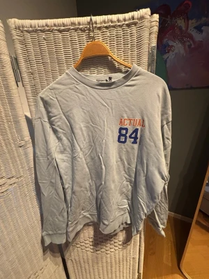 Grå sweatshirt med tryck från ASOS - Grå oversized sweatshirt med trycket 'ACTUAL 84' i orange och blått både fram och bak. Tröjan har rund halsringning och långa ärmar. Perfekt för en avslappnad och sportig stil.