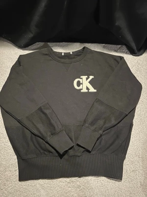 Svart sweatshirt från Calvin Klein - Hej jag säljer min Svart sweatshirt från Calvin Klein med broderad CK-logga på bröstet. Tröjan har rund halsringning, ribbade muddar vid ärmslut och nederkant samt en avslappnad passform. Perfekt för en casual och stilren look.