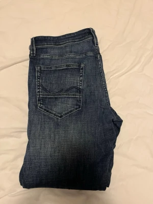 Mörkblå jeans från Jack & Jones - Säljer ett par mörkblå jeans från Jack & Jones med klassisk femficksdesign och snygga slitningar. Jeansen har normal passform och raka ben, samt tydliga kontrastsömmar. Perfekta till sneakers eller boots för en chill look.