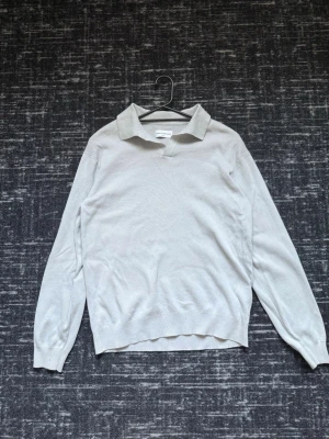 Ljusblå stickad polo - Snygg ljusblå stickad polo med klassisk krage och v-ringning. Tröjan har långa ärmar och ribbade muddar vid ärmslut och nederkant. Perfekt för lager på lager och enkel att matcha.