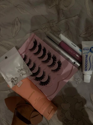 Set med lösögonfransar och mascara - Säljer ett kit med svarta, fylliga lösögonfransar i en rosa förpackning, samt en volymgivande mascara i silverhylsa. Ingår även ett lila läppglans med applikator. Perfekt för dig som vill ha en dramatisk ögonlook och glansiga läppar. Och en fot kräm! Sedan en liten tub tandkräm. Lite verktyg. Och en remover till fransar! Värde ca 400-500kr.