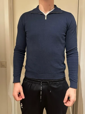 Marinblå stickad tröja half zip TeeShoppen - Snygg marinblå stickad tröja från TeeShoppen i storlek L. Tröjan har en klassisk half zip-dragkedja vid halsen och ribbade muddar vid ärmslut och nederkant. Perfekt till höst och vinter för en clean och stilren look.