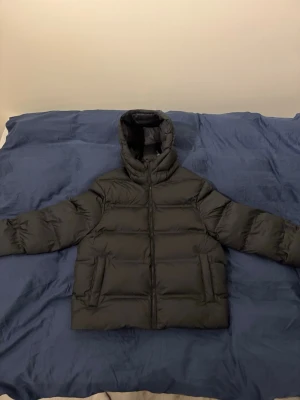 Zara jacka - Säljer en svart pufferjacka med huva och dragkedja framtill. Jackan är vadderad och har två stora fickor på sidorna. Perfekt för kalla dagar när du vill hålla dig varm och ändå se stilren ut.