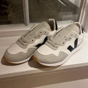 Veja sneakers vit/svart 37 - Säljer ett par Veja SDU Rec sneakers i storlek 37. Skorna är vita med svarta detaljer och har beige/grå mocka på ovandelen. De har snörning, platt sula och är tillverkade i syntet och mocka. Perfekta för dig som gillar stilrena och bekväma sneakers.