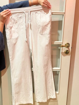 Vita lågmidjade linnebyxor - Säljer ett par vita linnebyxor med breda ben  och knytning. Byxorna har fickor fram och bak, samt ett litet broderat hjärta på ena bakfickan. Midjan är stretchig och i storlek XS-S. De är i perfekt skick💓