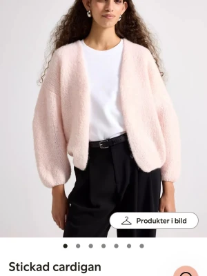 Ljusrosa stickad kofta - Supermjuk och fluffig ljusrosa stickad kofta med avslappnad passform och ballongärmar. Koftan är öppen framtill och har en mysig känsla, perfekt att slänga på sig över en t-shirt. Passar dig som gillar en chill och trendig look. Färgen är mörkare i verkligheten.