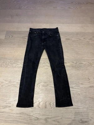 Svarta Nudie Jeans  - Säljer ett par svarta slim  jeans från Nudie Jeans. Klassisk femficksmodell med smal passform och diskret logga på bakfickan. Jeansen är i stretchigt denimtyg och har en mörk tvätt som ger en clean look. Frakt ingår ej. Hör gärna av dig ifall du har några frågor. 