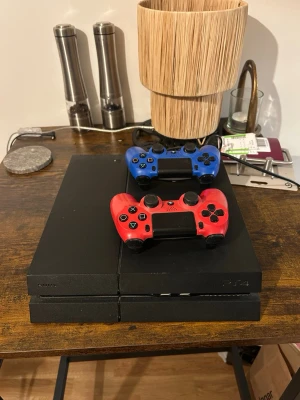 Ps4 med 2 kontroller - Säljer en PlayStation 4 (ps4) i fint skick med två DualShock 4 kontroller (en röd och en blå). Konsolen är välvårdad och fungerar utmärkt. Perfekt för spelkvällar och underhållning. Inga synliga större repor eller skador.