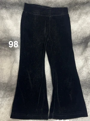 Svarta byxor i sammet - Säljer ett par svarta byxor i mjuk sammet. Byxorna har en bred resår i midjan och utsvängda ben för en snygg siluett. Perfekta för dig som gillar en trendig och bekväm stil.🌸 Fint använt skick. Storlek 98