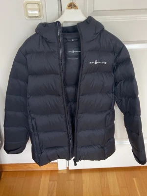 Svart dunjacka Sail Racing JR Gravity - Säljer en svart Sail Racing JR Gravity dunjacka med huva och dragkedja. Jackan har en stilren look med logga på bröstet och huvan. Fylld med RDS-certifierat ankdun (80% dun, 20% fjäder) och yttermaterial i nylon.   Bra skick på jackan. Se defekter på bild. 