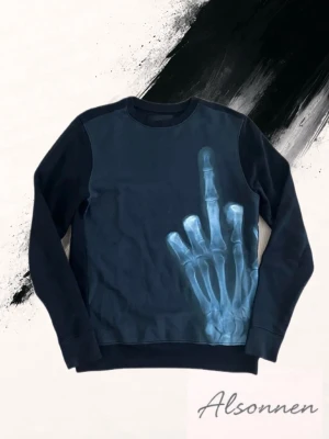 Svart sweatshirt Limitato - Cool svart sweatshirt från Limitato med ett unikt röntgenmotiv av en hand som visar långfingret på framsidan. Tröjan har rund hals, långa ärmar och är tillverkad i mjuk bomull. Perfekt statement piece för dig som vill sticka ut.