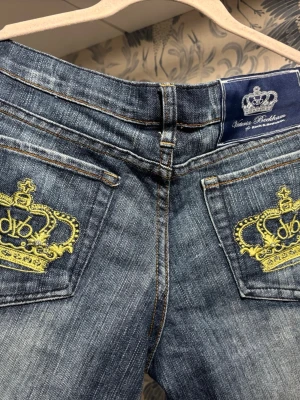 Victoria Beckham x Rock & Republic jeans - Snygga blå jeans med bootcut från Victoria Beckham x Rock & Republic. Bakfickorna har broderade gula kronor som ger en unik touch. Klassisk femficksmodell i jeansmaterial och normal passform. Saknar dock knapp vid guld men fungerar bra med bälte!