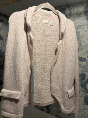 Ljusrosa kofta från Odd Molly - Supersöt ljusrosa och vit kofta från Odd Molly med diskret mönster, broderad logga på ärmen och grå knytband bak. Koftan är stickad, har långa ärmar och en mysig krage. Perfekt för lager på lager och chill vibes.