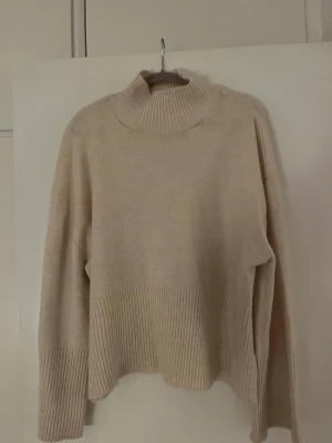 Beige stickad polotröja Gina Tricot - Mysig beige stickad polotröja från Gina Tricot i storlek S. Tröjan har ribbade detaljer vid hals, ärmslut och nederkant samt en loose passform. Perfekt för lager-på-lager under kyliga dagar.