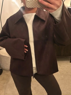 Brun mockajacka med dragkedja - Säljer en brun mockajacka med rak passform och bred krage. Jackan har långa ärmar och stängs med dragkedja framtill. Materialet är mjukt och ger en snygg look, perfekt att styla med jeans. Enkel och stilren design utan synliga detaljer. Storlek L men passar en S/M men är prefekt för en mer Baggy look, helt slutsåld på veromoda. Köptes för 600 kr och endast använt en gång men pris kan diskuteras