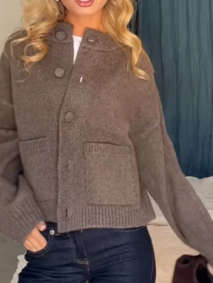 Brun stickad kofta med stora knappar - Mysig brun stickad kofta med stora matchande knappar framtill och två rejäla fickor. Koftan har en rak, lite loose passform och ribbade detaljer vid ärmslut och nederkant. Perfekt för lager på lager under kyliga dagar.
