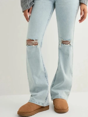 Ljusblå bootcut jeans med slitningar - Säljer ett par ljusblå jeans med bootcut passform och slitna hål över knäna. Jeansen har en klassisk femficksdesign och cool detalj med röd broderad söm på bakfickan. Tillverkade i jeansmaterial och sitter midwaist. De är uppsydda så de passar någon som är 160-165cm men går att sprätta upp så de passar längre personer. Använda ca 2 gånger