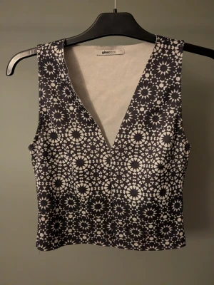 Svartvit mönstrad linnetopp Gina Tricot - Säljer en snygg linnetopp från Gina Tricot i storlek S. Toppen är svartvit med ett unikt geometriskt mönster och har v-ringning. Den är ärmlös och har en figurnära passform, perfekt att styla med jeans eller kjol.