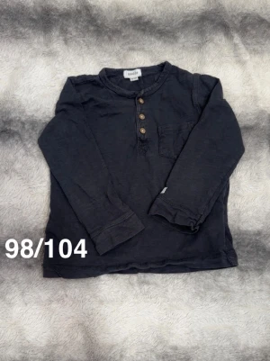Grå långärmad t-shirt Newbie - Grå långärmad t-shirt från Newbie med rund hals, bröstficka och tre träknappar framtill. Perfekt för en avslappnad och stilren look.🌸 Fint använt skick. Storlek 98/104
