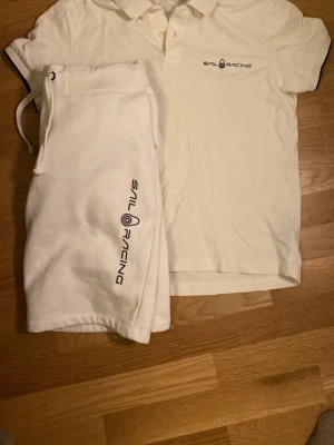 Vita Sail Racing shorts med snörning - Vita shorts från Sail Racing med snörning i midjan och logga längs benet. Klassisk och sportig look med relaxed fit, perfekta för sommardagar. Tillverkade i mjuk bomull för maximal komfort. (Tröjan är storlek S och shortsen är storlek M men även känns som S)