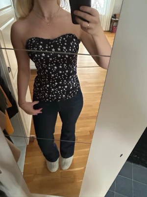 Svart tubtopp med vita stjärnor - Säljer en svart tubtopp med vita stjärnor i olika storlekar. Toppen är figurnära och axelbandslös, perfekt för dig som vill ha en cool och trendig look. Materialet känns mjukt och stretchigt, vilket gör den bekväm att bära hela dagen.