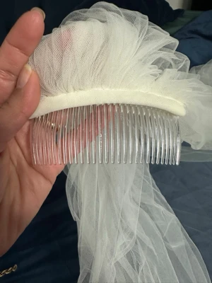 Vit brudslöja med spets och pärlor - Säljer en lång, vit brudslöja med broderade spetsdetaljer och blommiga mönster. Slöjan har insydda pärlor och fästs enkelt med en transparent kam. Perfekt för dig som vill ha en romantisk och elegant look på bröllopet. Längd ca 2,5- 3 m, crèmefärgad 