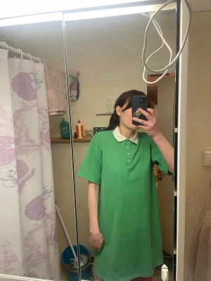 Grön pikéklänning från Carin Wester - Säljer en grön pikéklänning från C.W. i storlek S. Klänningen har vit krage, knappar framtill och är tillverkad i ett bomullsliknande material. Oversized passform och kort ärm, perfekt för en avslappnad look. Liten fläck framtill knappt märkbar, samt i kragen som förhoppningsvis går bort med lite vittvättmedel. 