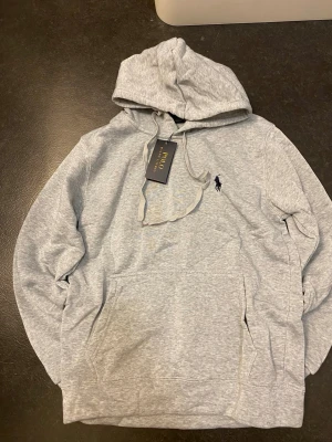 Polo Ralph Lauren grå hoodie - Stilren grå hoodie från Polo Ralph Lauren med klassisk logga på bröstet. Mjuk och bekväm passform, perfekt till vardags. Storlek-S